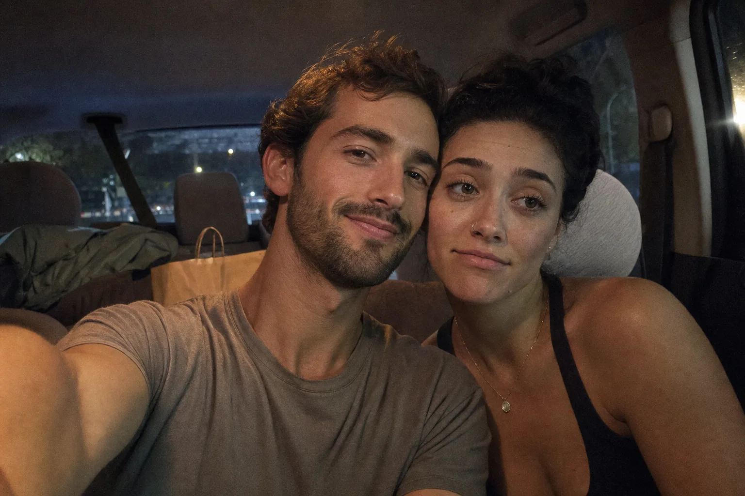 Two people take a parked-car selfie after a casual date, one warm and the other uncertain.