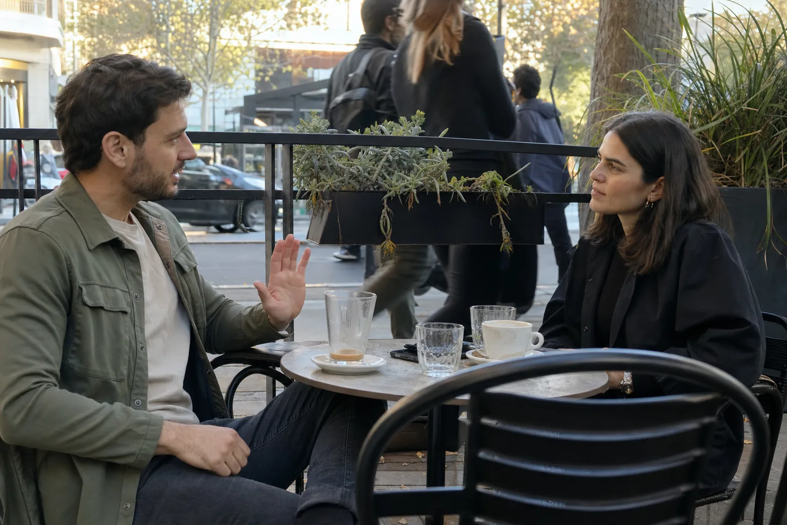 A man makes a calm pause gesture while setting a boundary with his partner at an outdoor cafe.