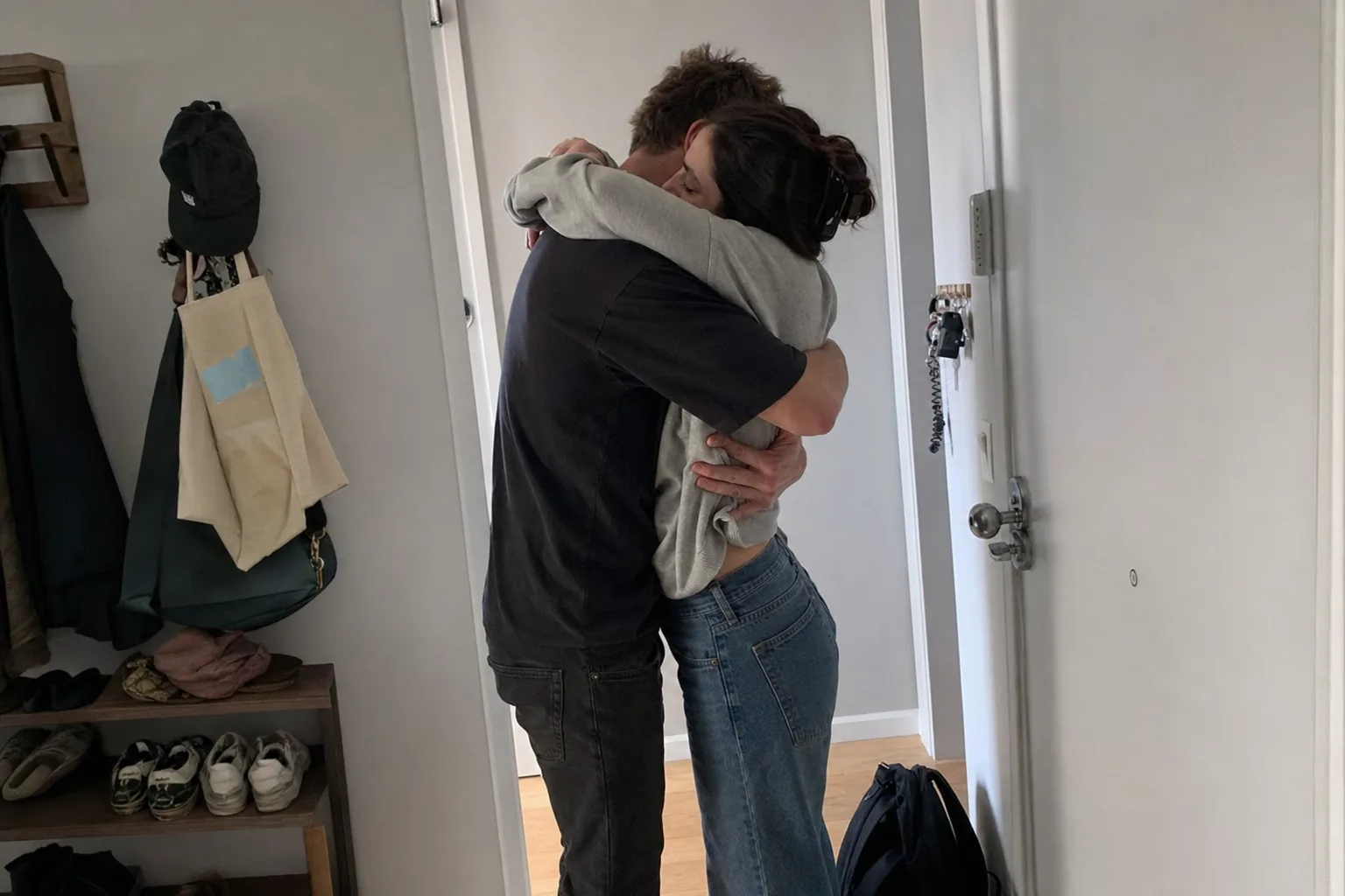 A couple shares a long goodbye hug in an apartment doorway.