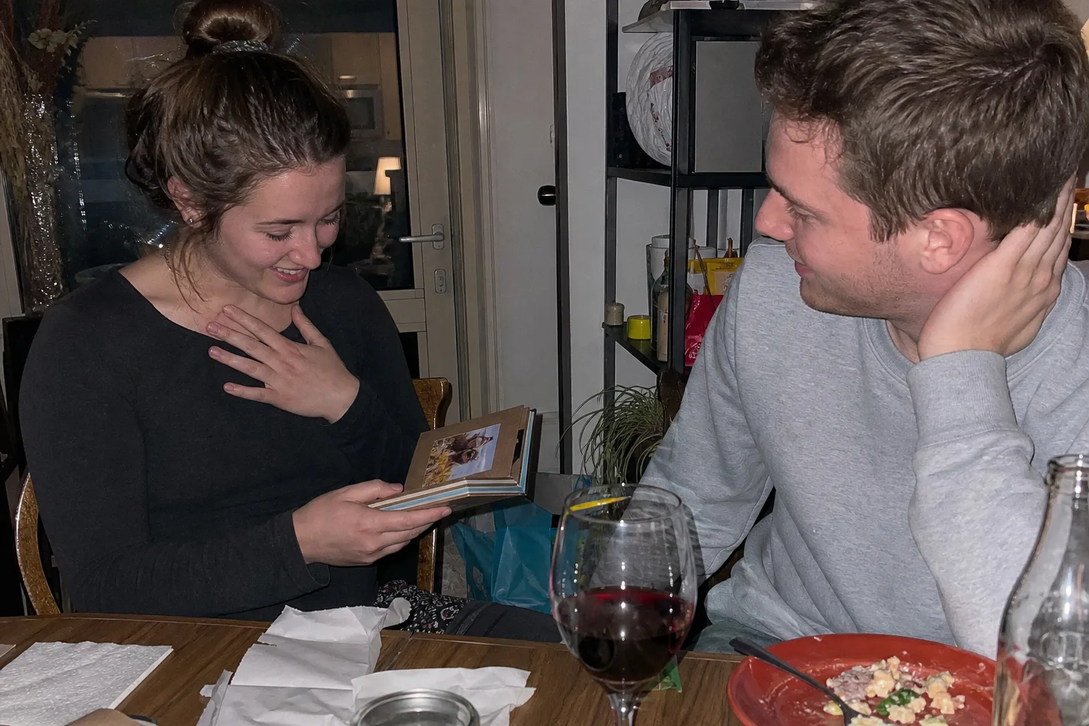 A person gives their partner a small handmade photo album as a thoughtful gift.